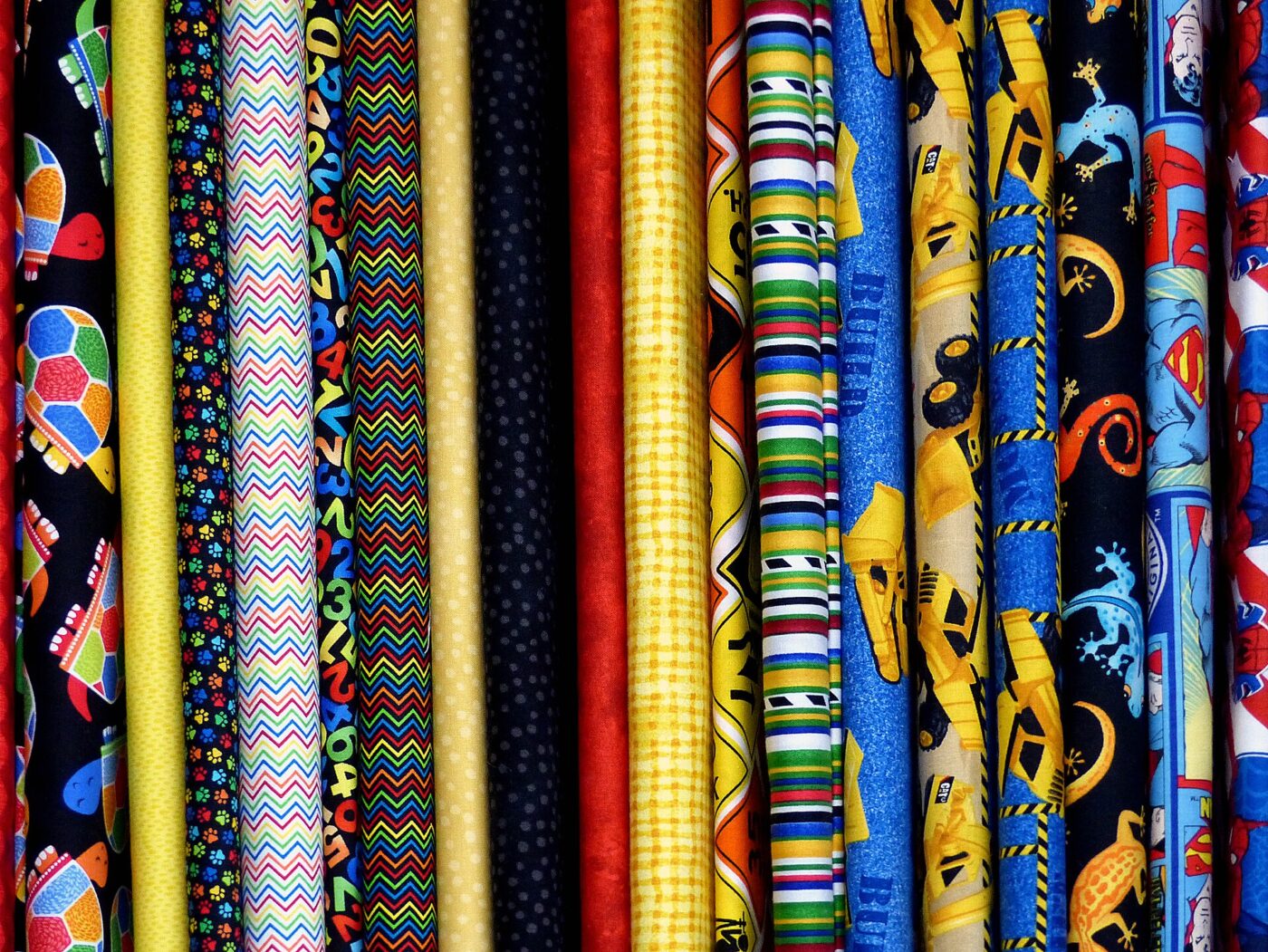 Upright bolts of brightly patterned fabric with stripes, zigzags and novelty prints lined up side by side