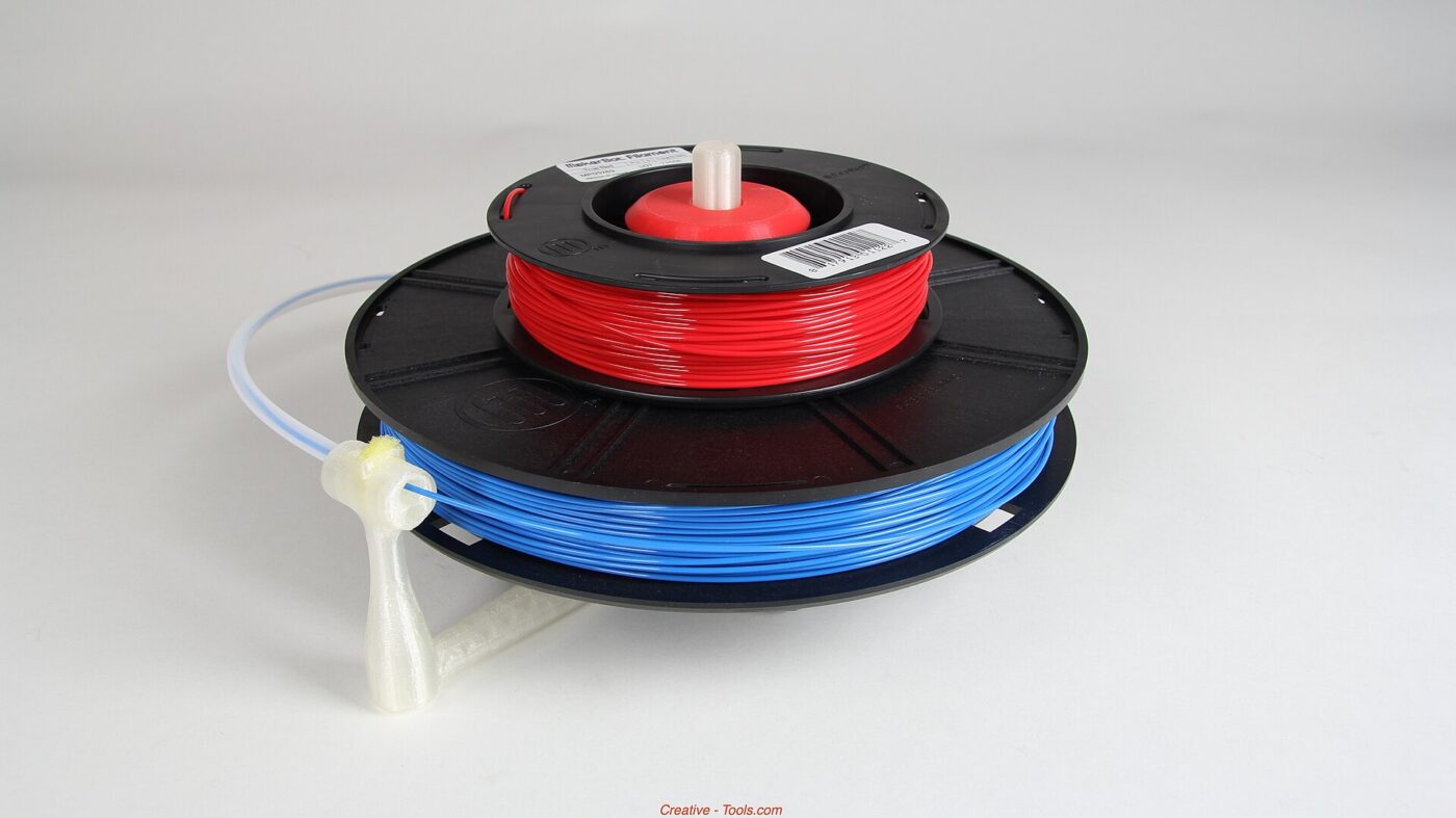 Two spools of red and blue printer filament on a printed stand-alone holder.