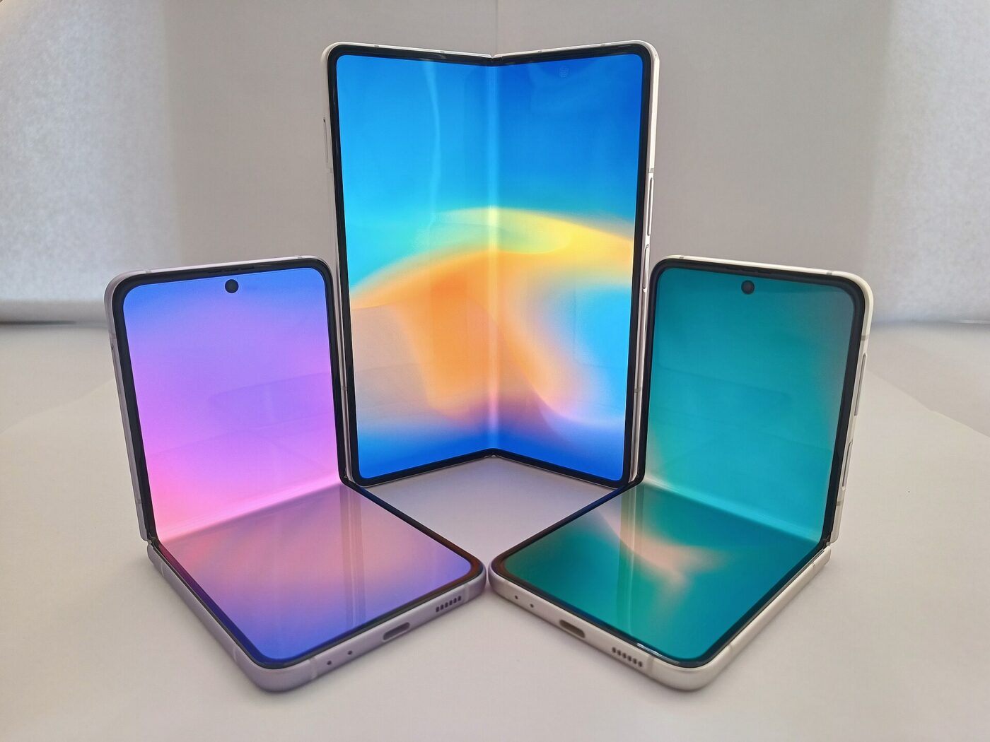 Two clamshell foldable phones and one book-style foldable standing open with colorful screens