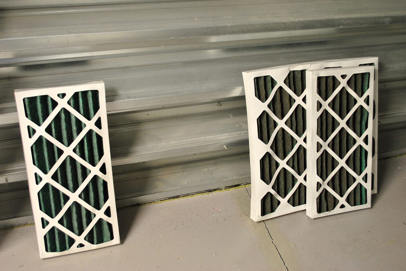 Two pleated panel air filters with cardboard frames standing against a metal wall