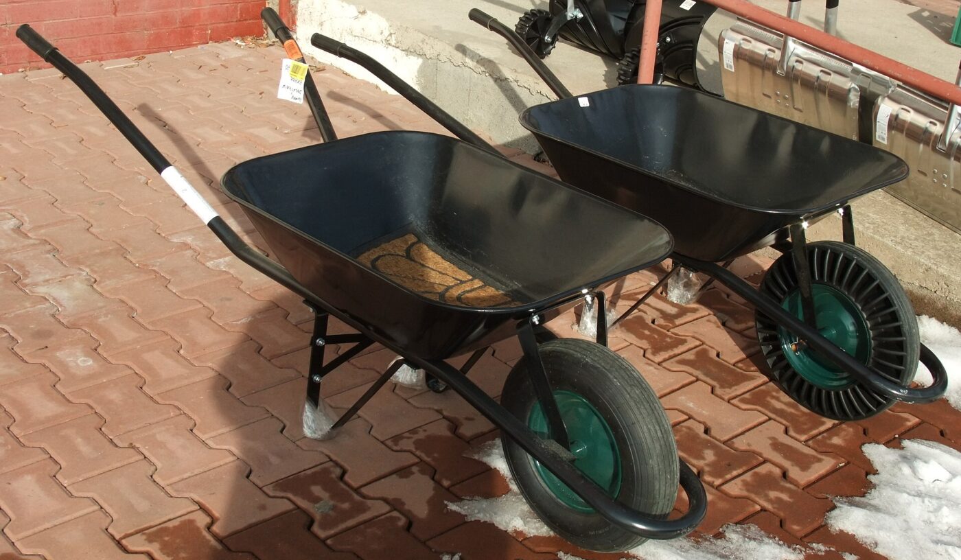 Two black steel-tray wheelbarrows with pneumatic tires parked on a paved yard.