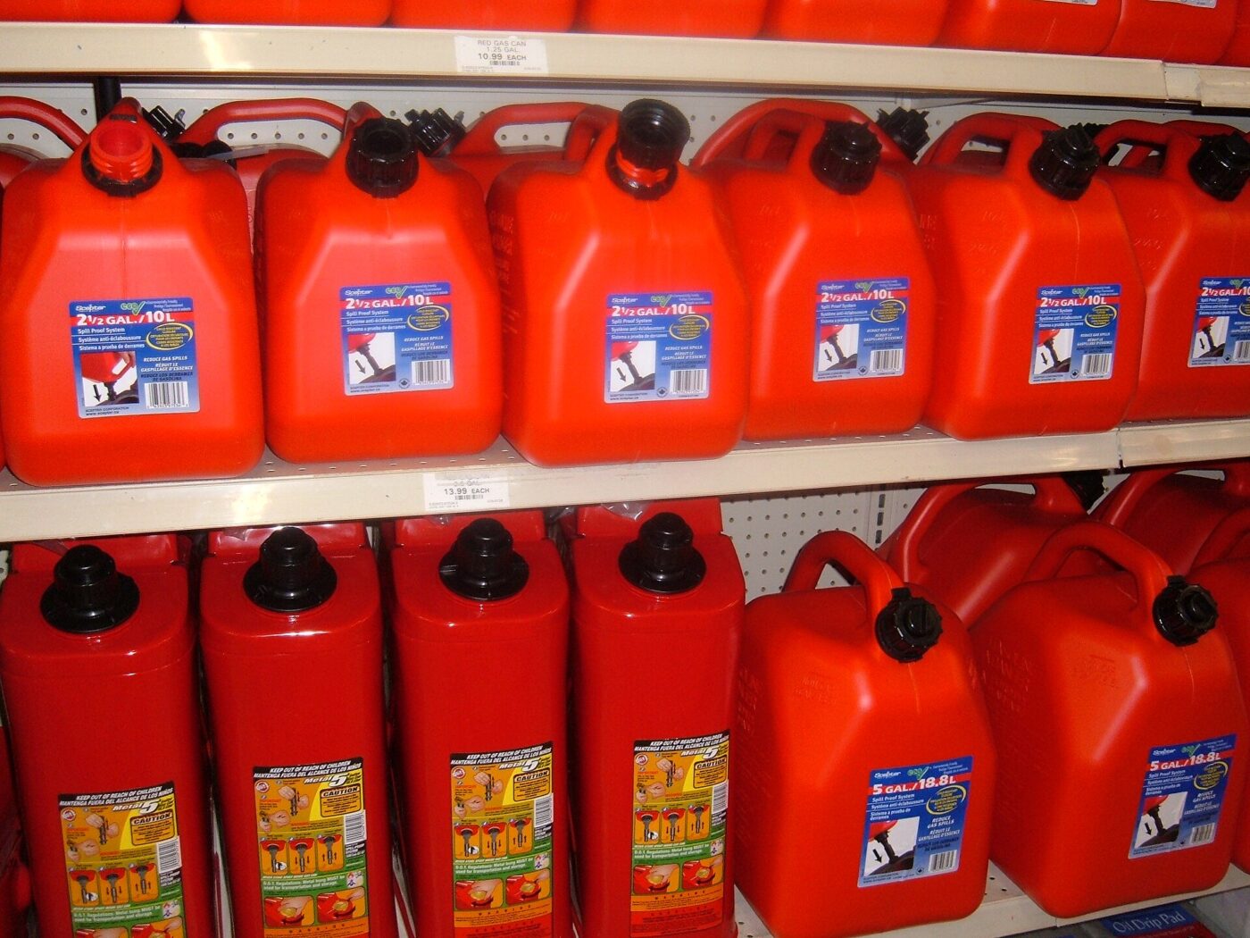 Red plastic portable gasoline cans with spouts stacked on shelves in a store.
