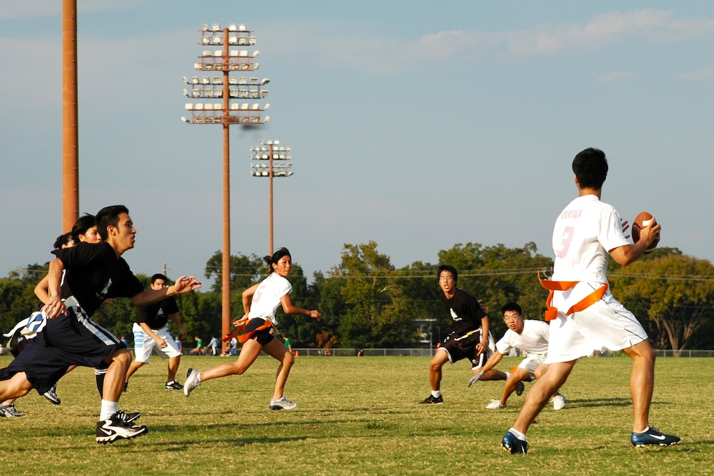 Players wearing flag belts chase the ball carrier during a flag football game on a grass field