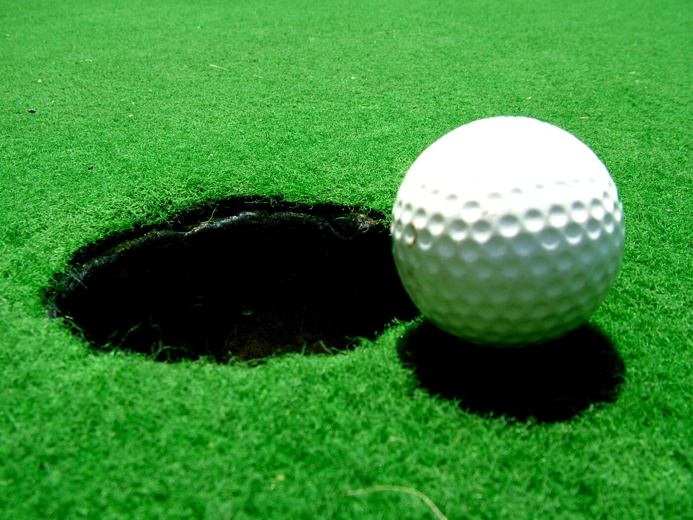 A golf ball sitting at the edge of the hole on a putting green.