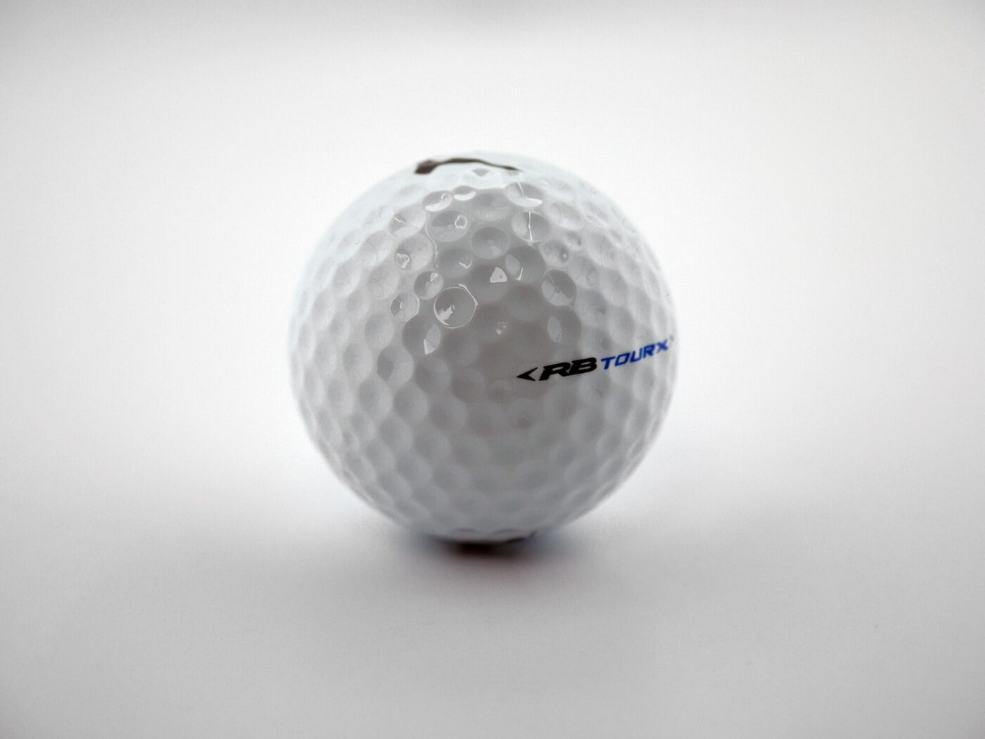 A white golf ball on a plain studio background, its dimple pattern in focus.