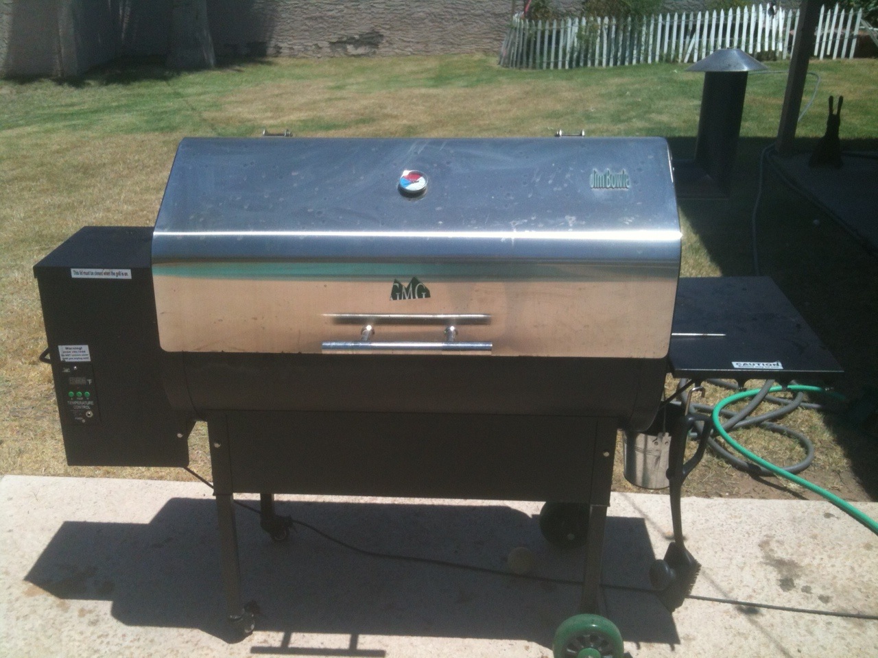 A stainless steel pellet grill with its hopper on the side, set up on a backyard patio