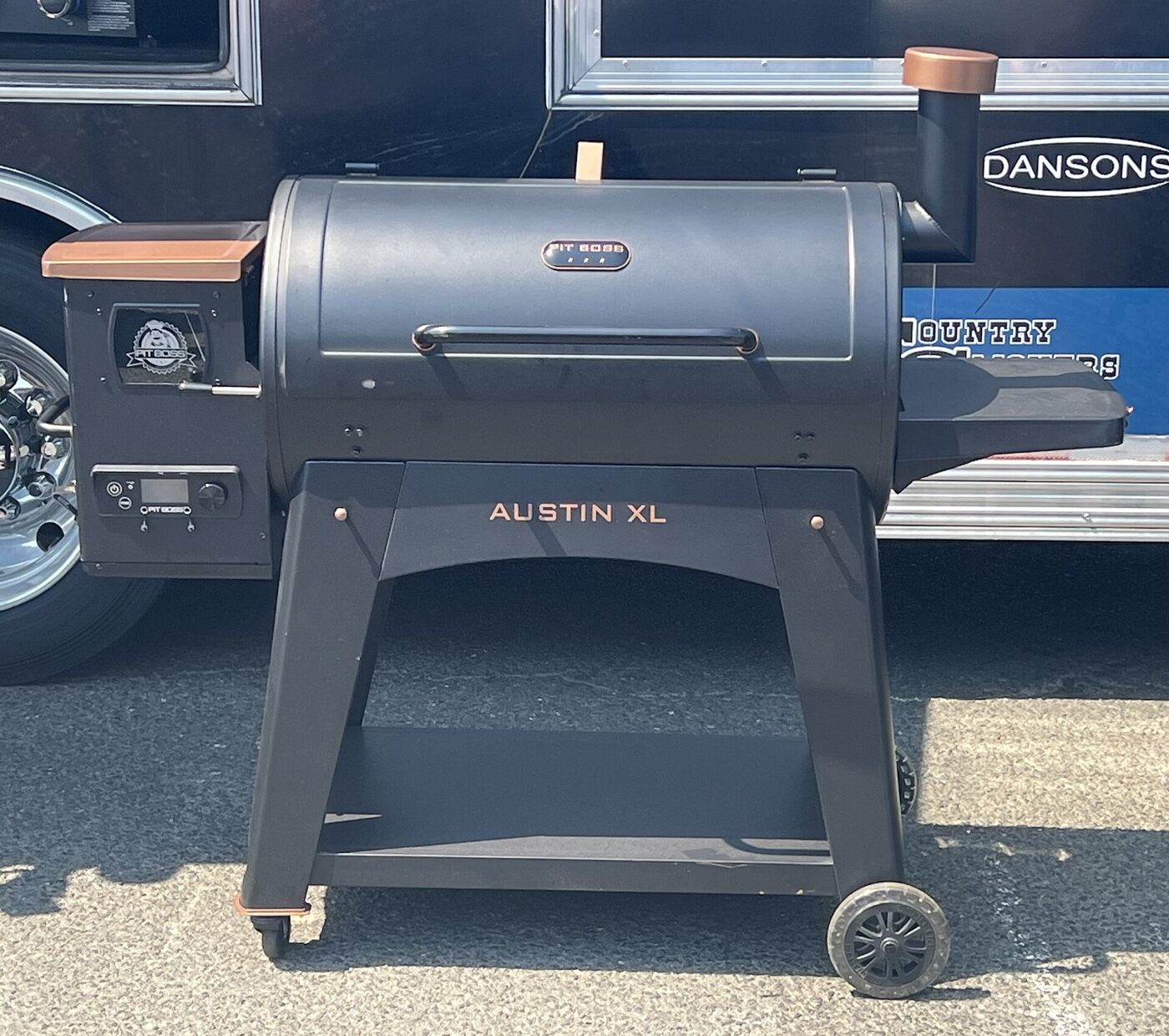 A black wood pellet grill with a side pellet hopper and digital controller, parked outdoors