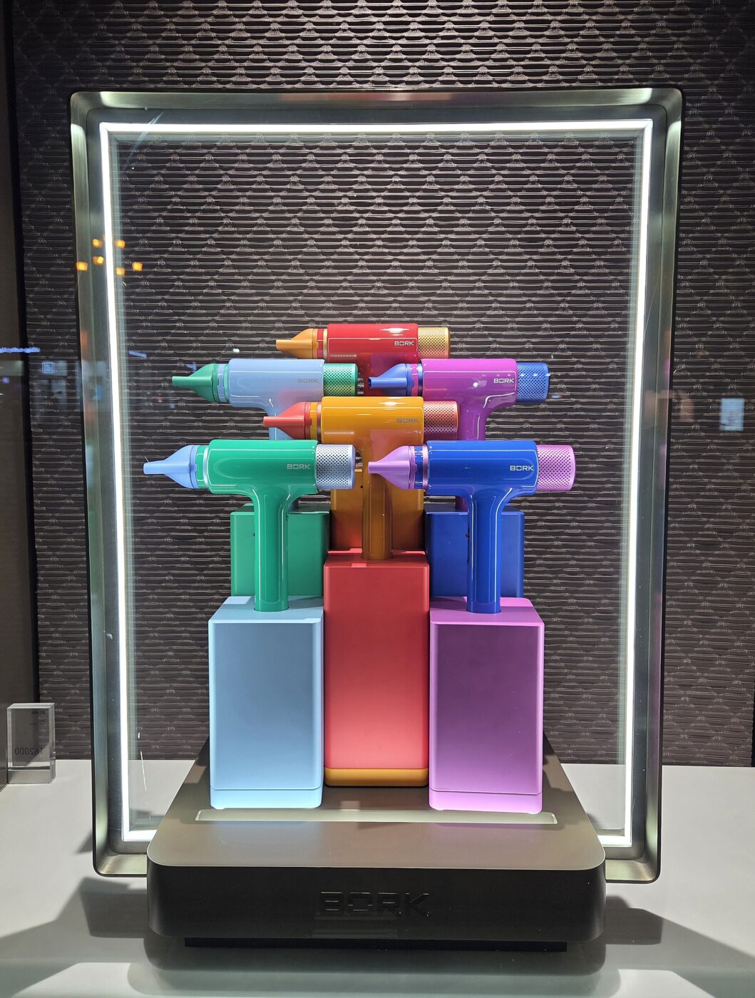 Handheld hair dryers in several colors arranged on a lit retail display stand