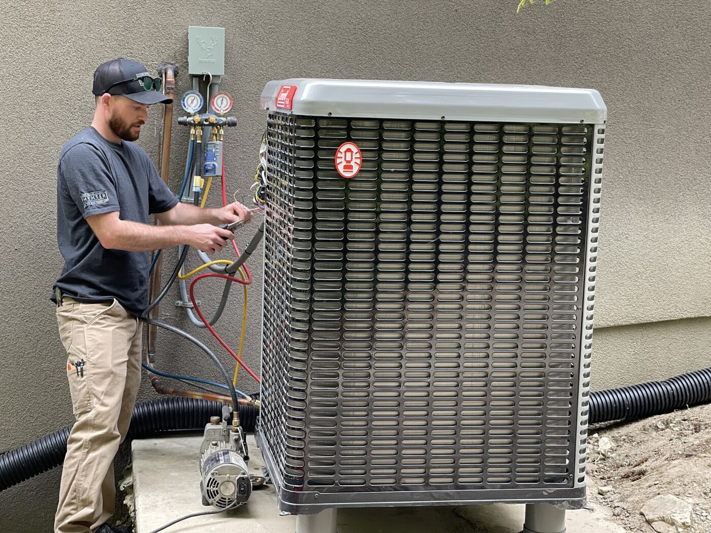 A technician connects refrigerant gauges and a vacuum pump to an outdoor heat pump unit during installation