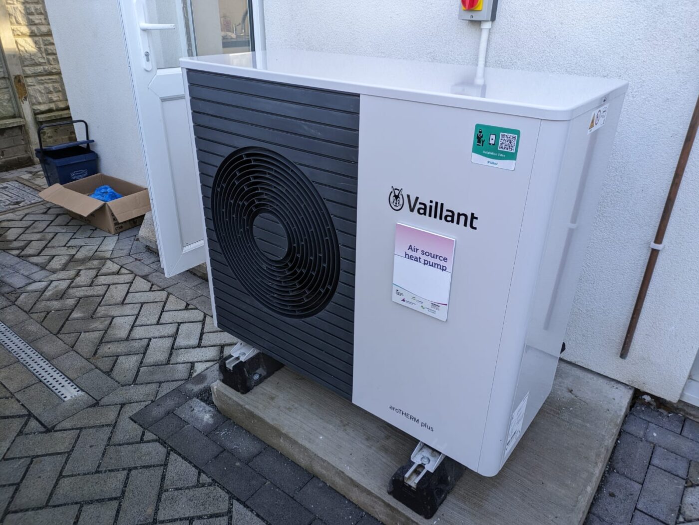An air source heat pump outdoor unit on a concrete base beside the back door of a house