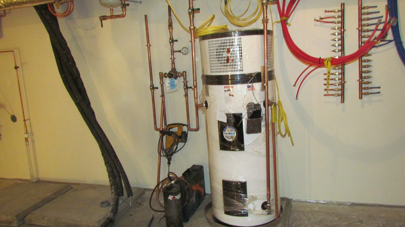 A heat pump water heater during installation, with copper lines and wall manifolds behind