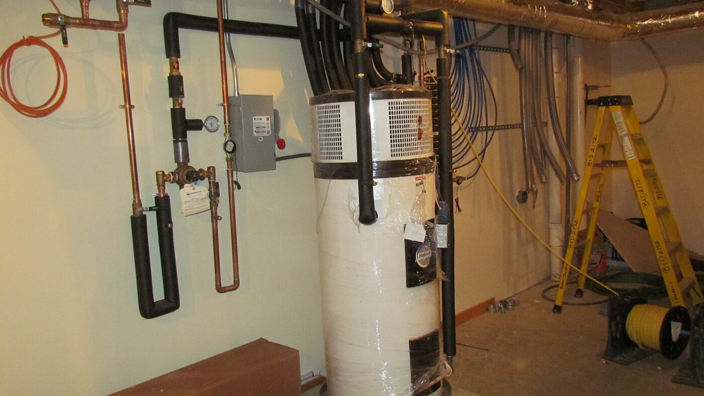A heat pump water heater installed in a mechanical room, with its copper connections