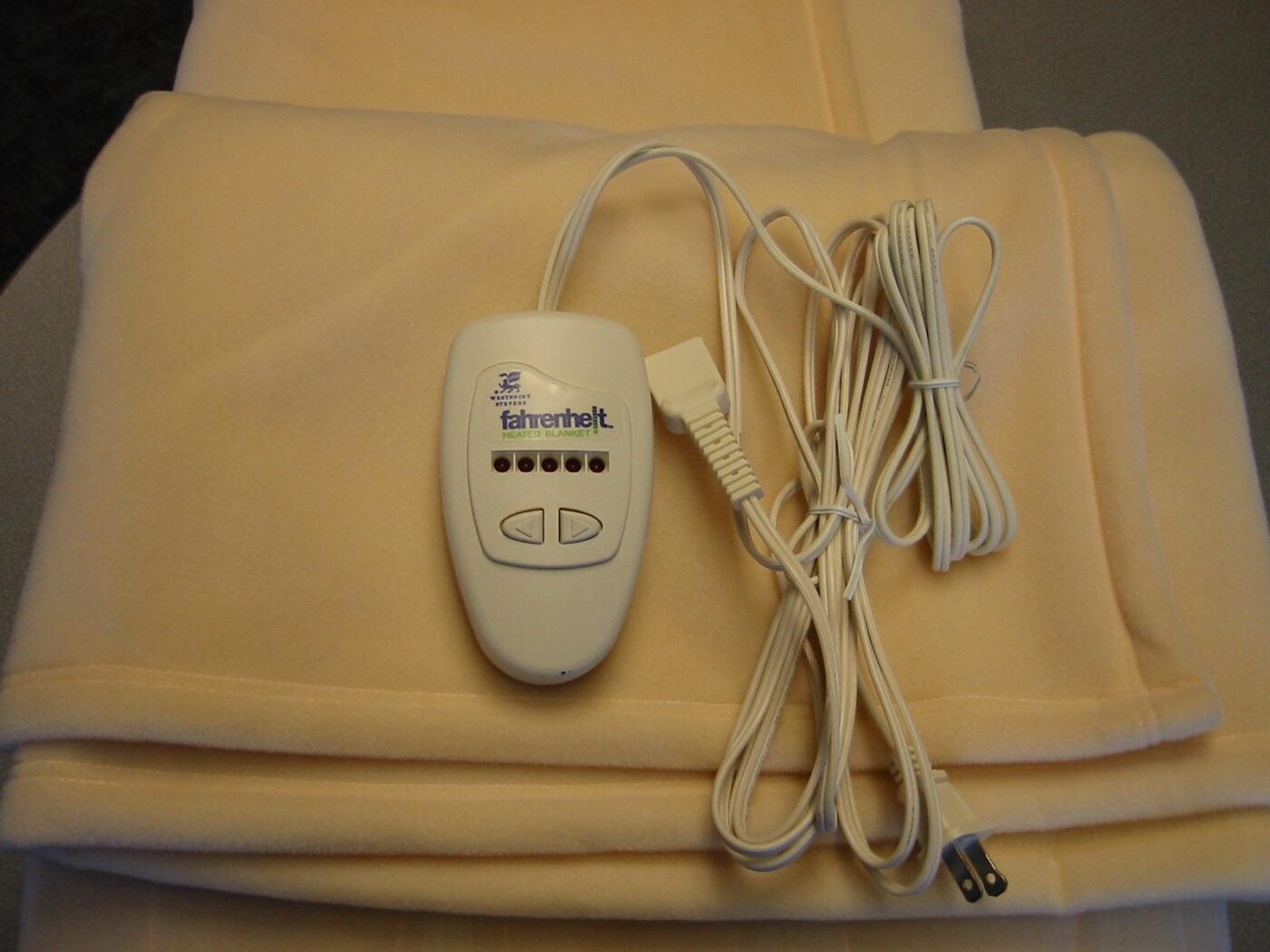 A folded cream electric blanket with its corded hand controller resting on top