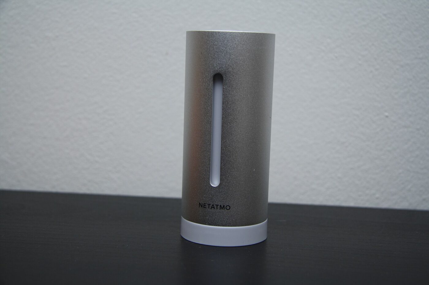 A slim cylindrical indoor air sensor standing on a table against a pale wall