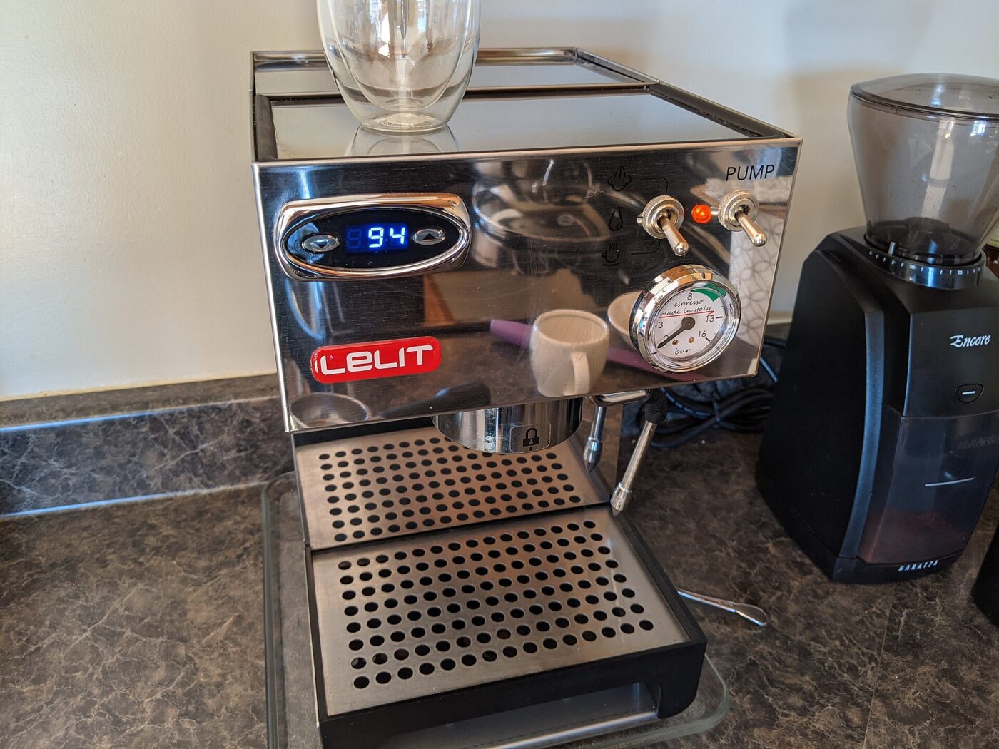 A semi-automatic home espresso machine with a pressure gauge beside a burr grinder on a kitchen counter