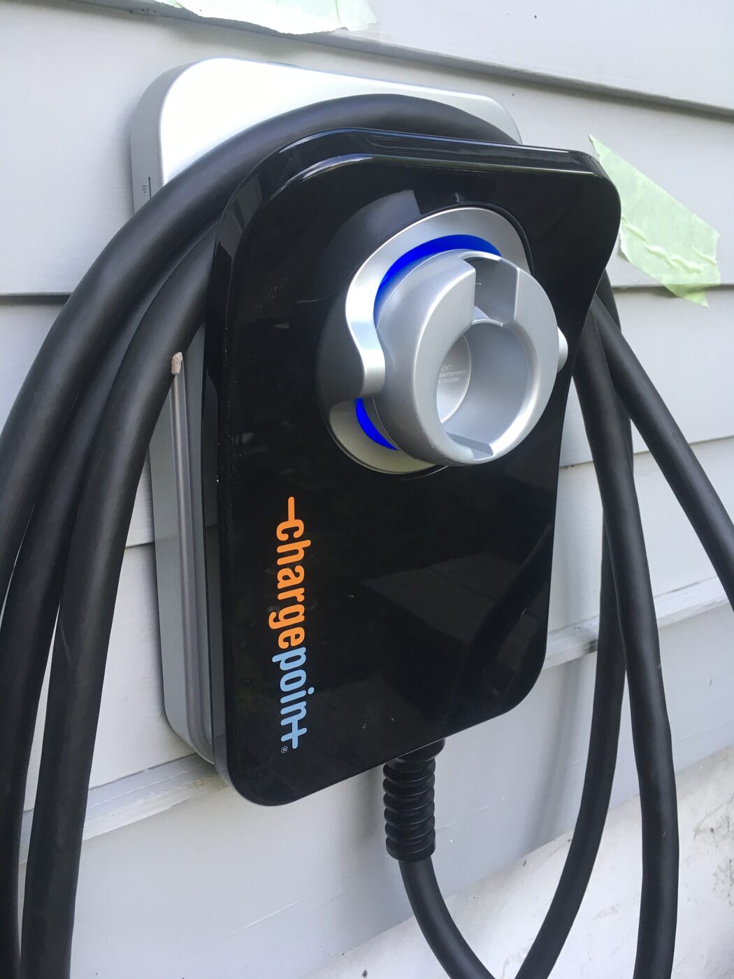 A home charging unit mounted on house siding, connector holstered and cable coiled beside it