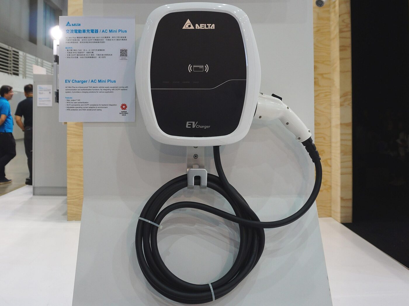 A wall-mounted electric vehicle charger, its connector and coiled cable hanging from the unit