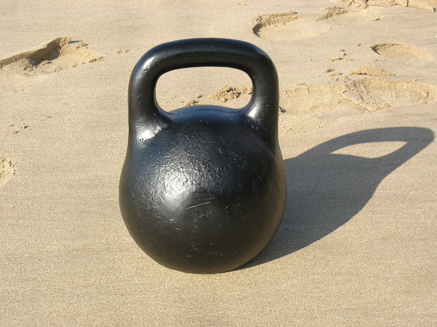 A black iron kettlebell casting a long shadow on sunlit sand