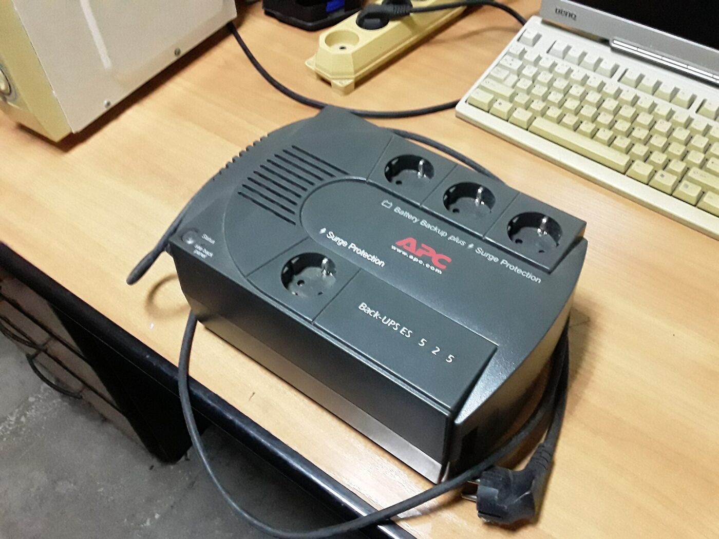 A black desktop battery backup unit sitting on a desk beside a computer keyboard