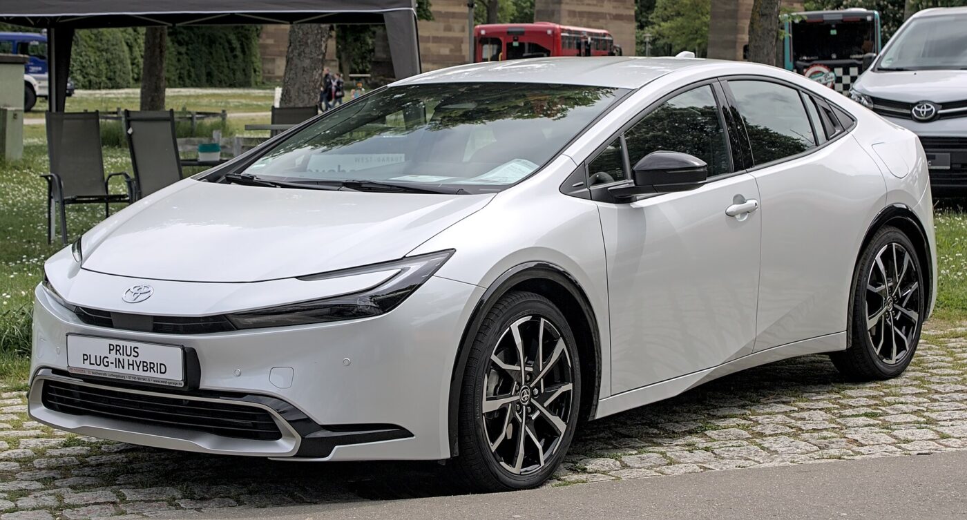 A white Toyota Prius Plug-in Hybrid parked on cobblestones, with its name on the front plate