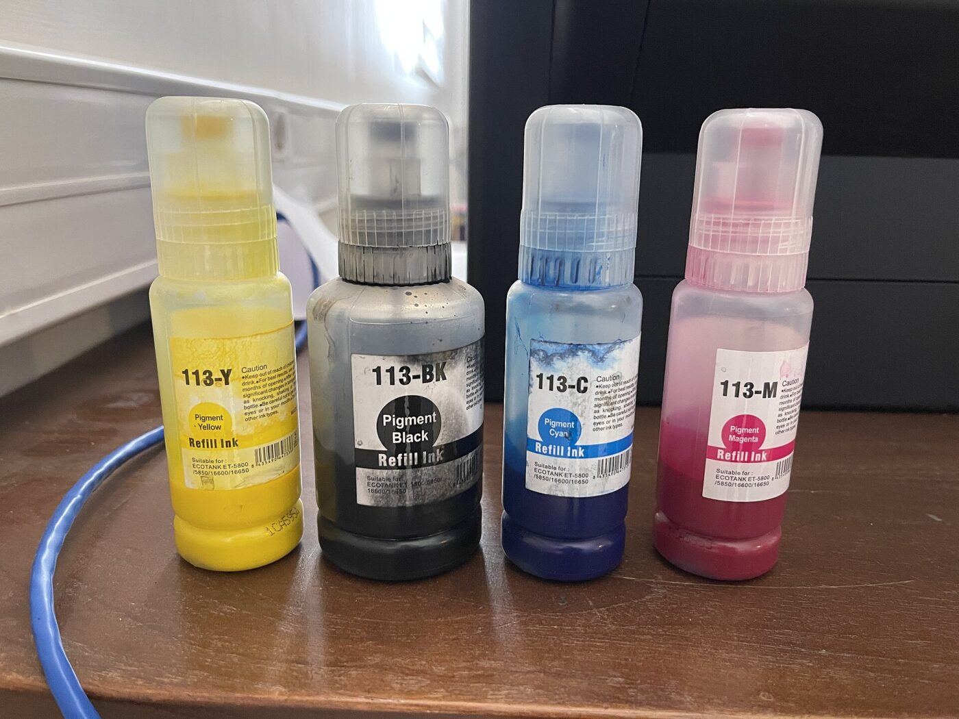Four sealed ink refill bottles in yellow, black, cyan and magenta standing on a table