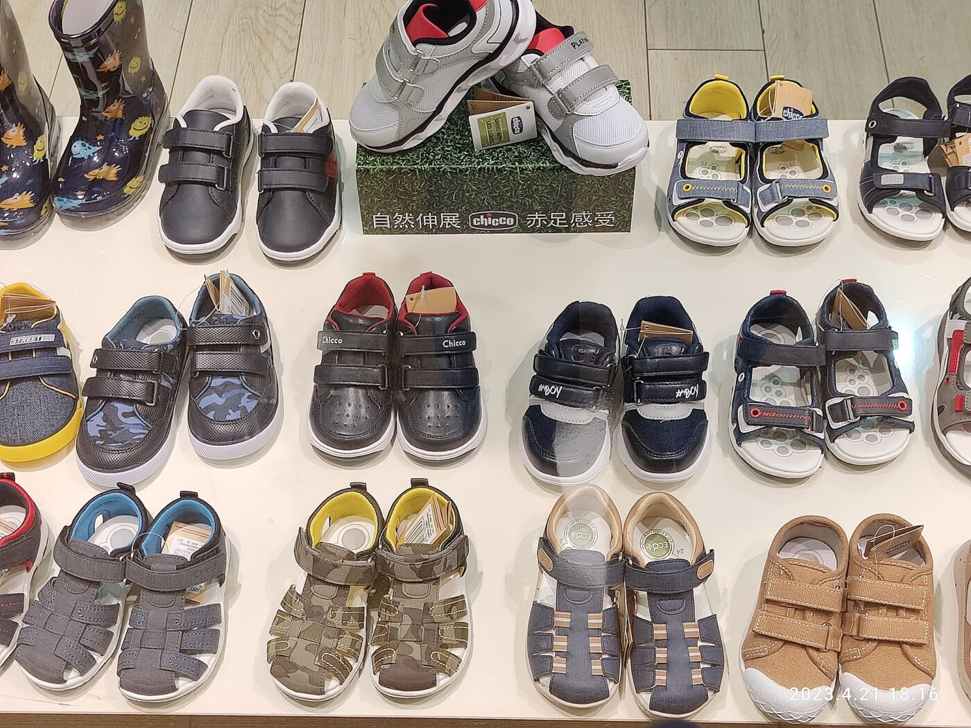Small children's shoes and sandals lined up in rows on a store display shelf.