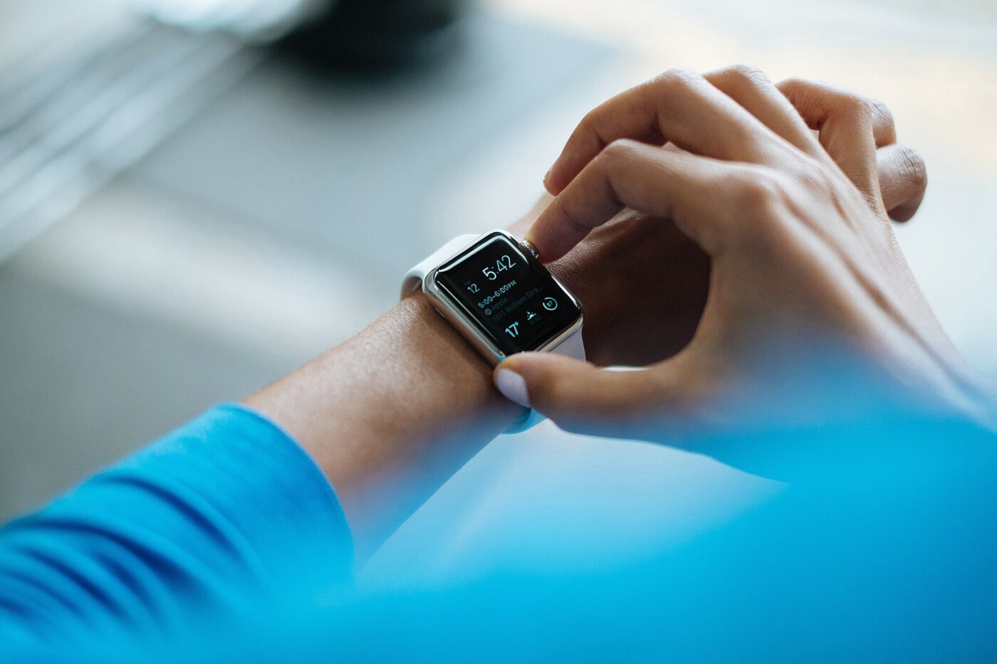 Person tapping the screen of a square-faced smartwatch with a white band on their wrist