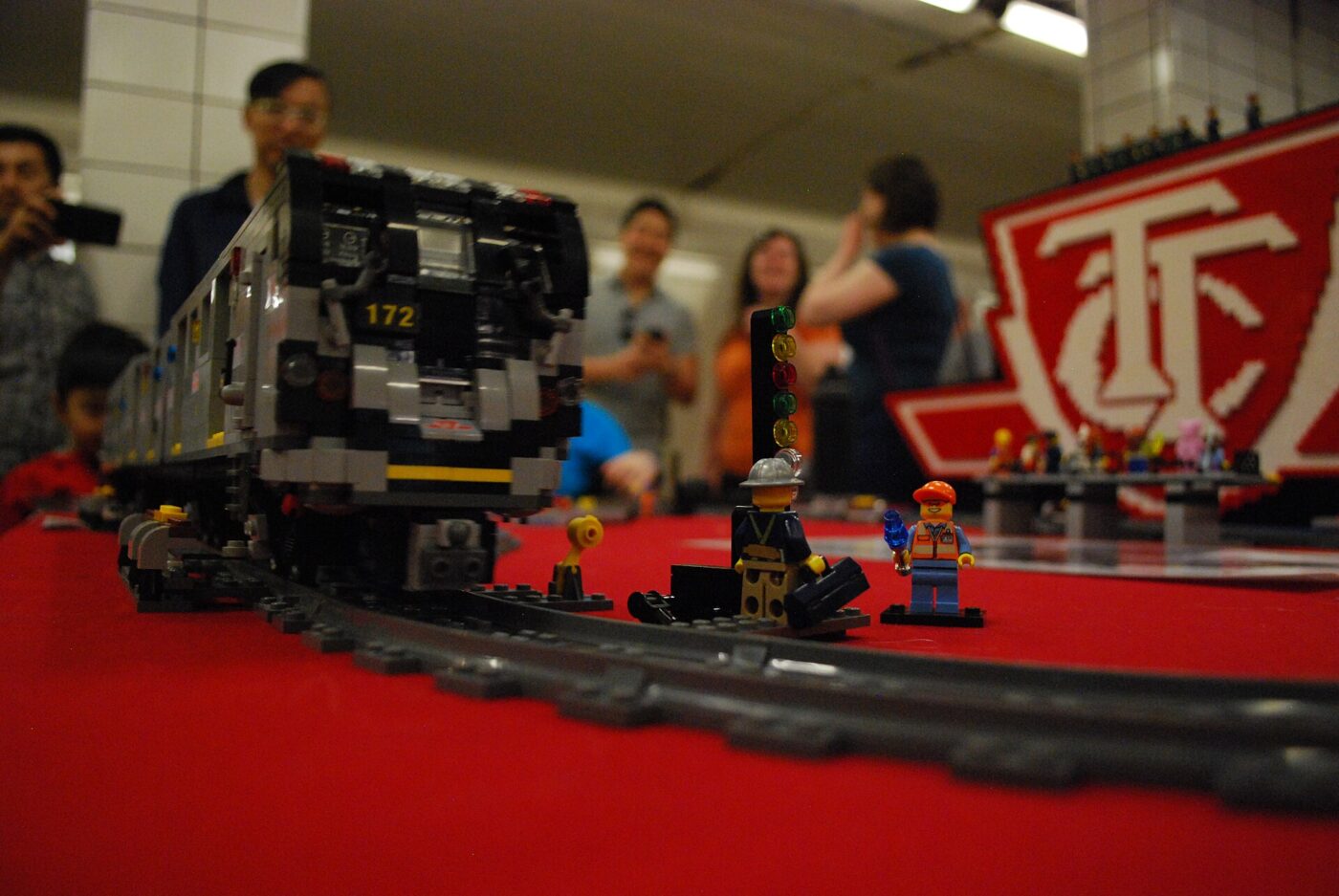 A detailed LEGO model subway train on a display track as visitors look on in the background
