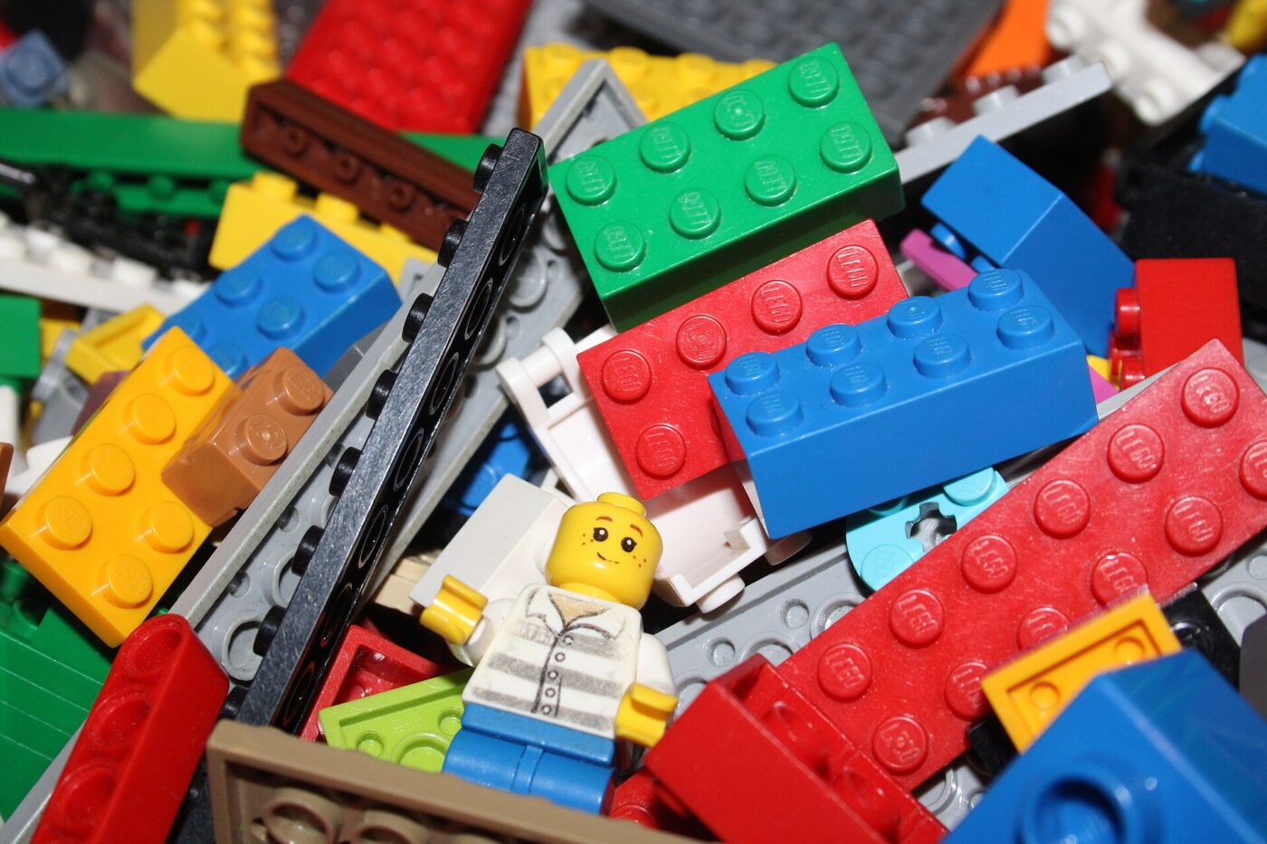 A pile of colorful LEGO bricks with a smiling LEGO minifigure lying among them