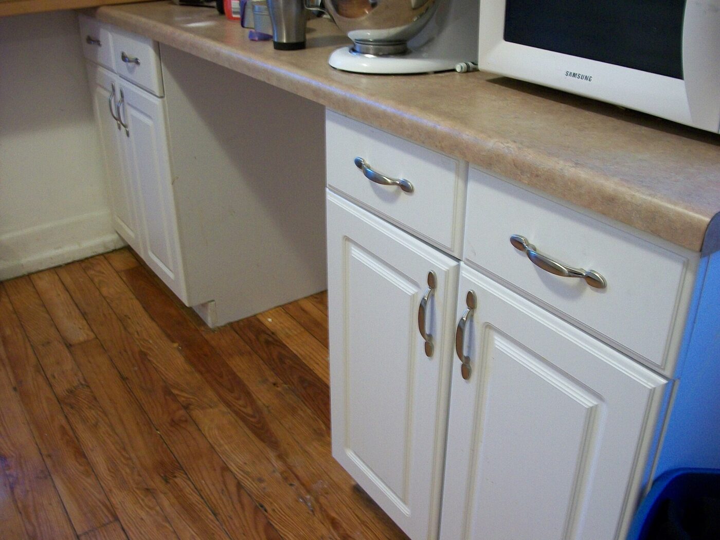 White kitchen cabinets and drawers installed along a counter above a wood floor