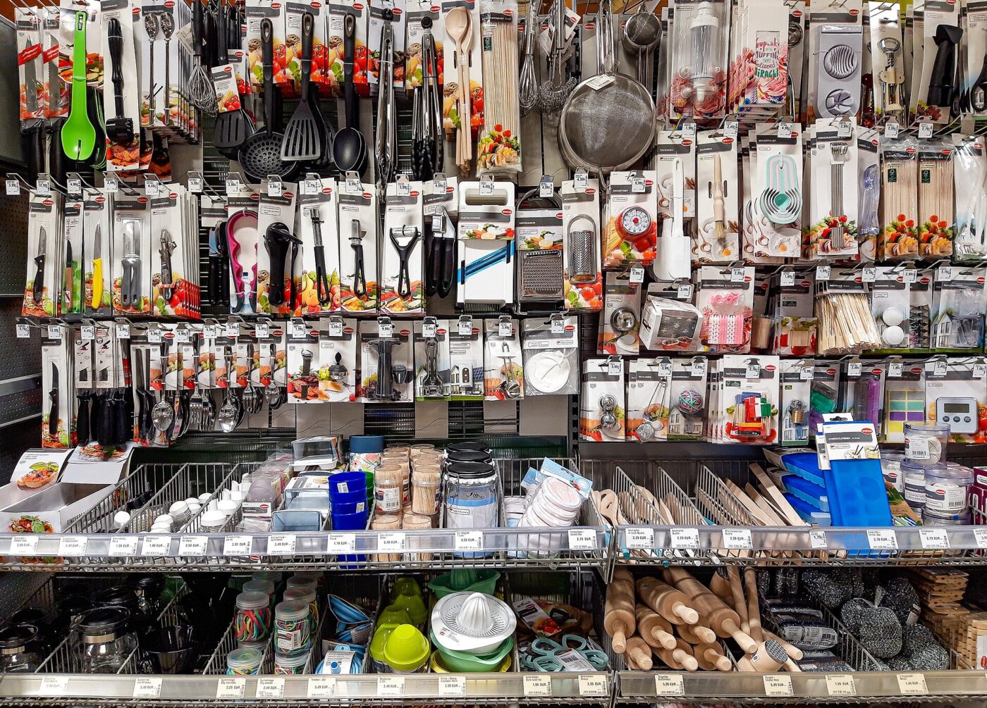 Packaged kitchen utensils and gadgets hang on a store wall above shelves of rolling pins and bowls