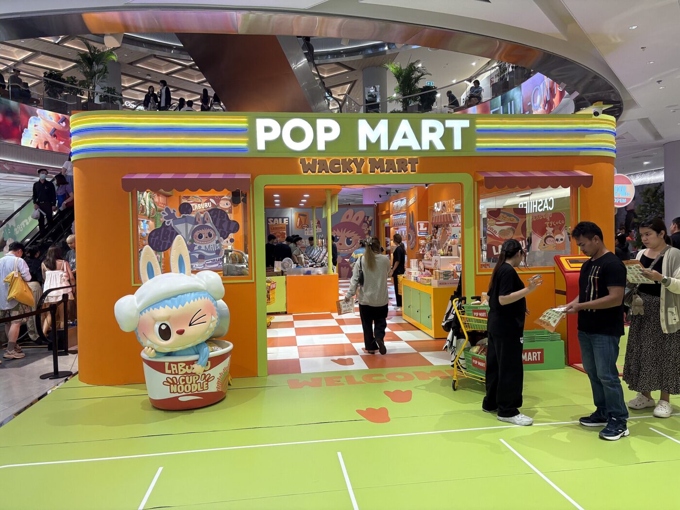 Shoppers at a Pop Mart pop-up shop inside a mall, with a large character figure at the entrance