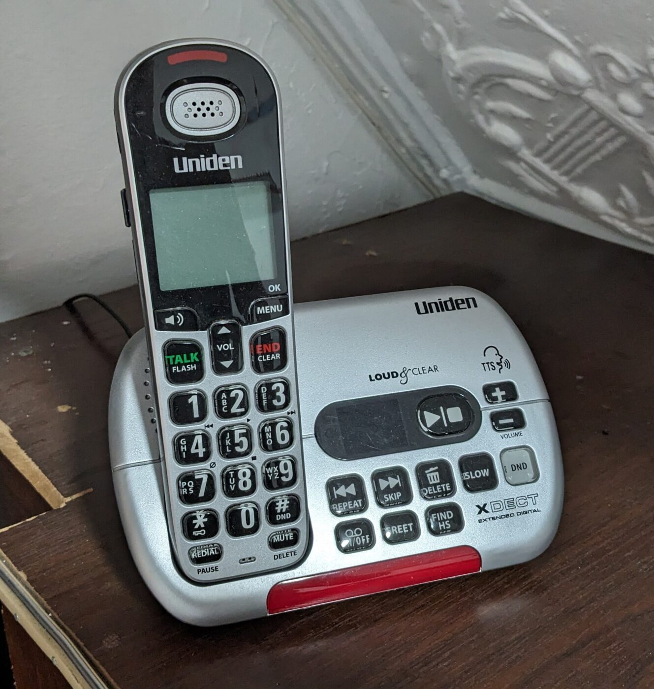 A cordless home phone with large buttons resting in its charging base on a table