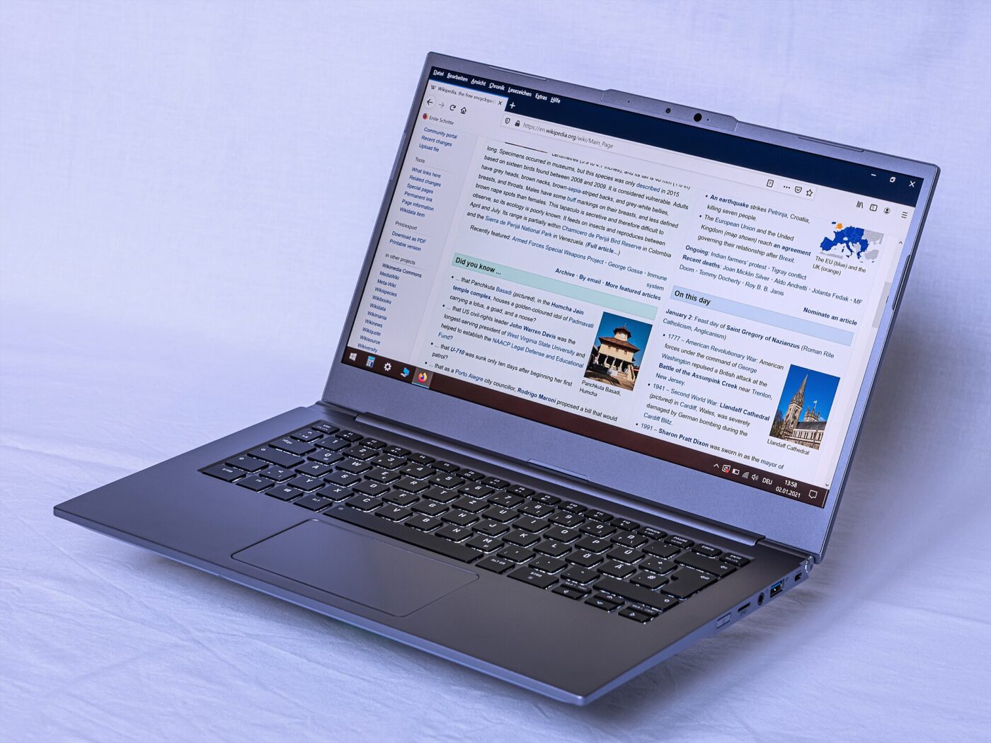 Slim gray laptop open at an angle on a pale blue backdrop, with a web page on screen