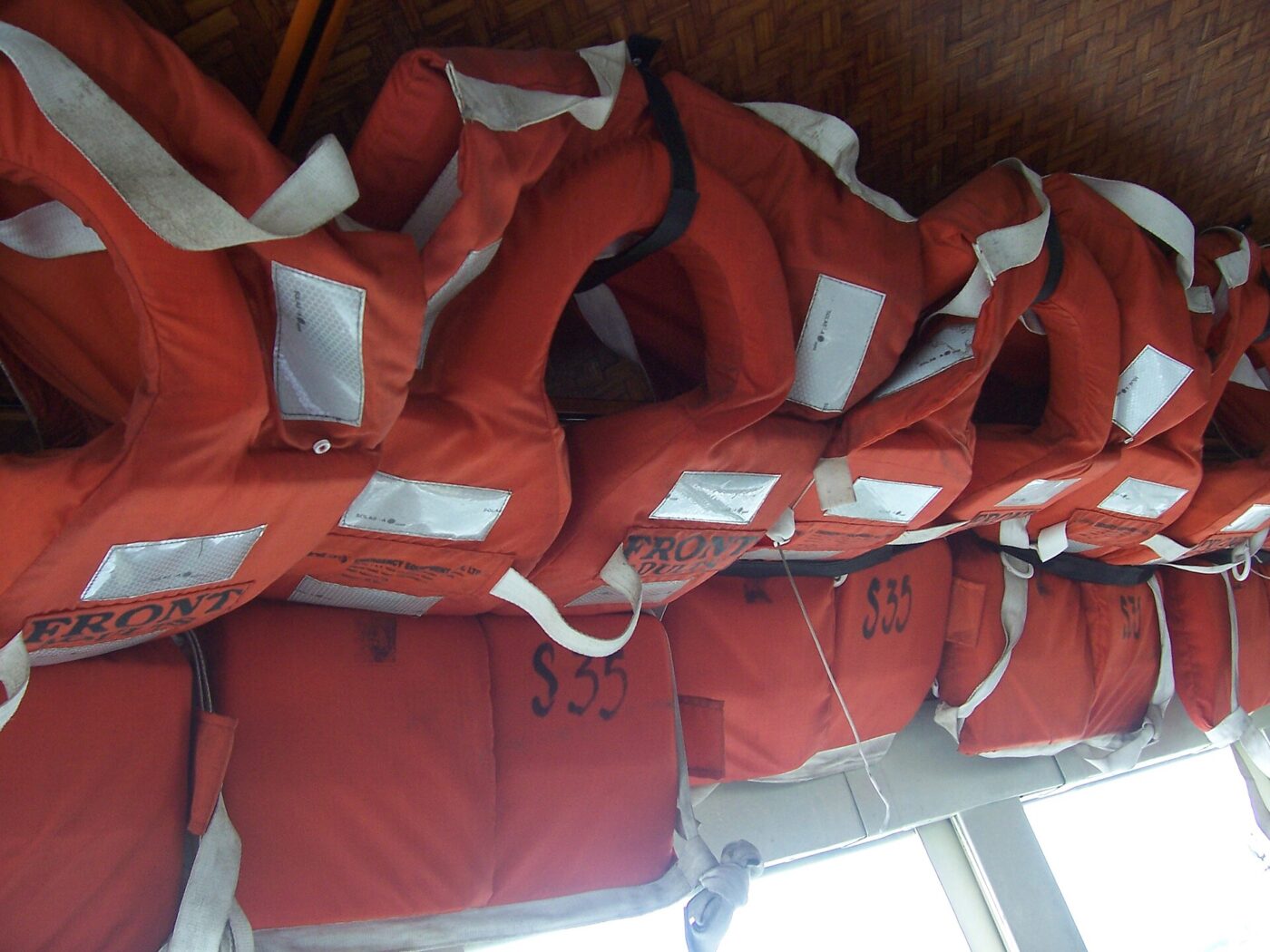 Rows of orange foam life jackets stowed on a rack aboard a passenger boat.