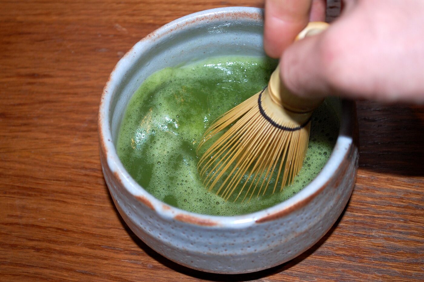 A bamboo whisk frothing bright green matcha tea in a ceramic bowl