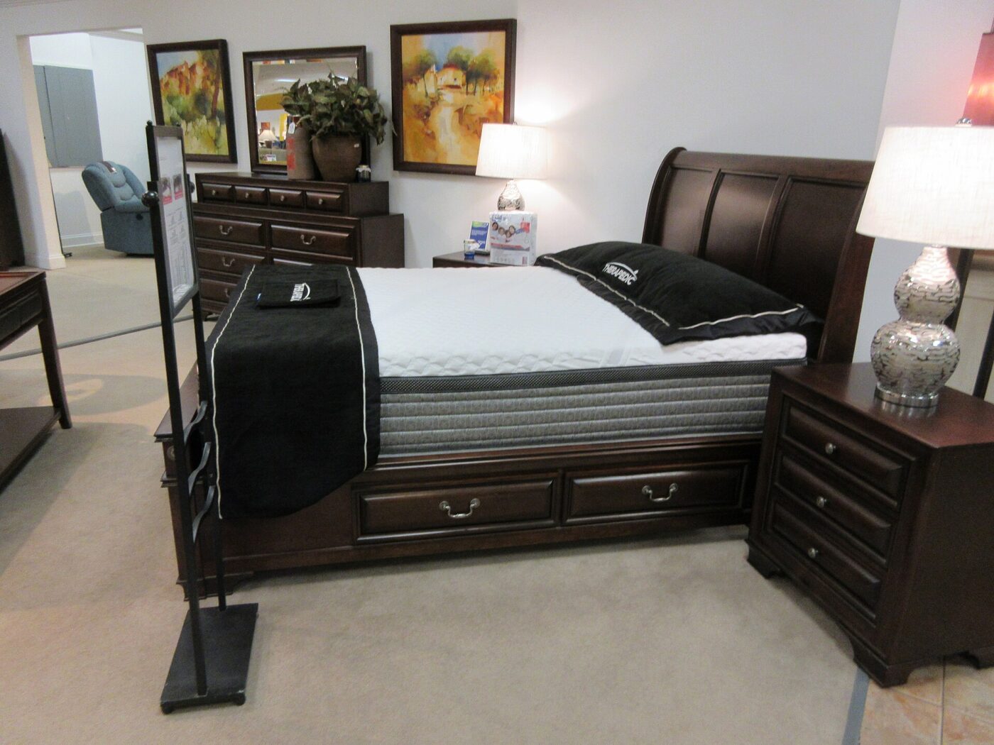 A mattress on a dark wooden bed frame in a furniture store showroom, with nightstands and lamps