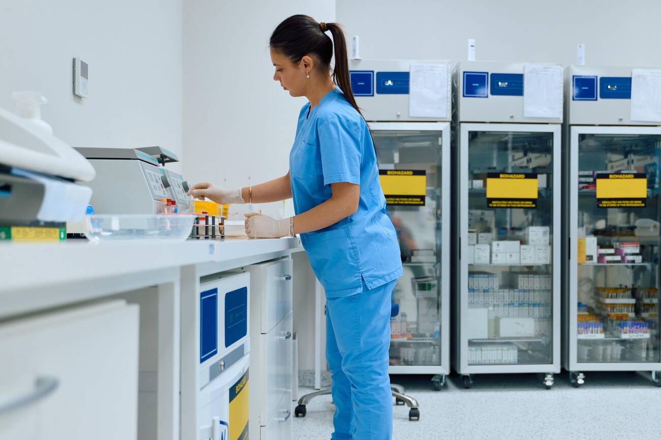 A lab worker in a blue scrub top and pants handles samples in a laboratory
