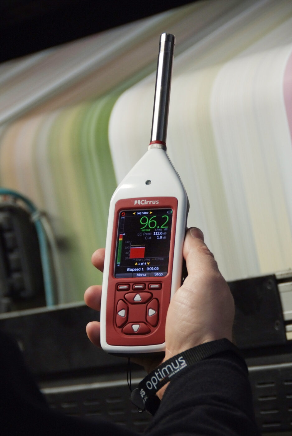A hand holding a handheld sound level meter that displays a decibel reading.