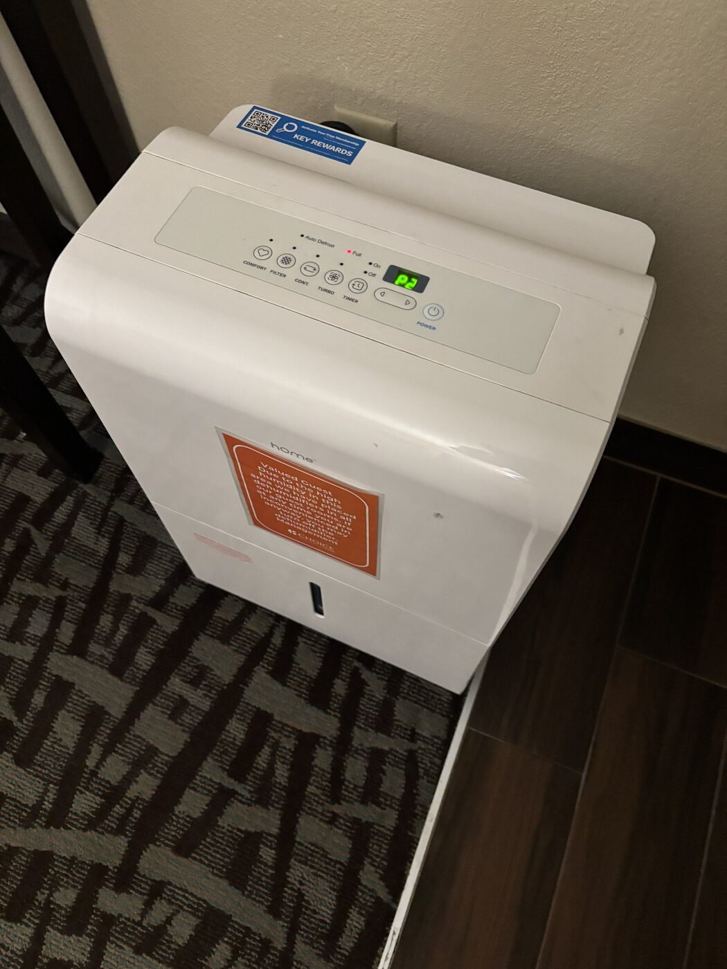 A portable dehumidifier with a control panel on top, standing on the floor of a bedroom.