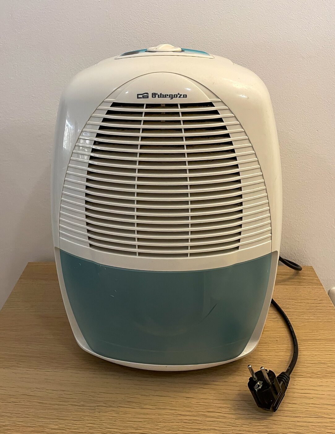 A portable dehumidifier with its water tank at the base and its plug set beside it.