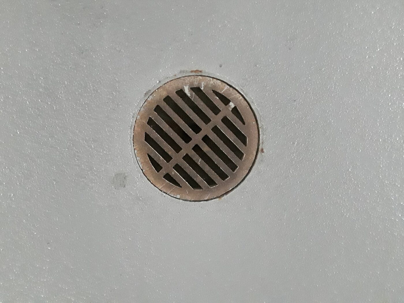 A round metal floor drain set into a bare concrete floor.