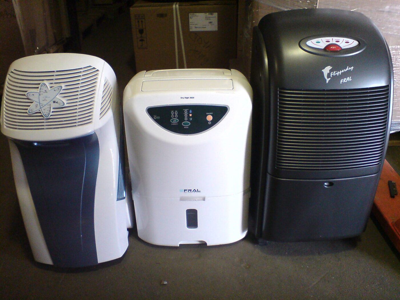 Three portable dehumidifiers of different makes standing side by side on a floor.