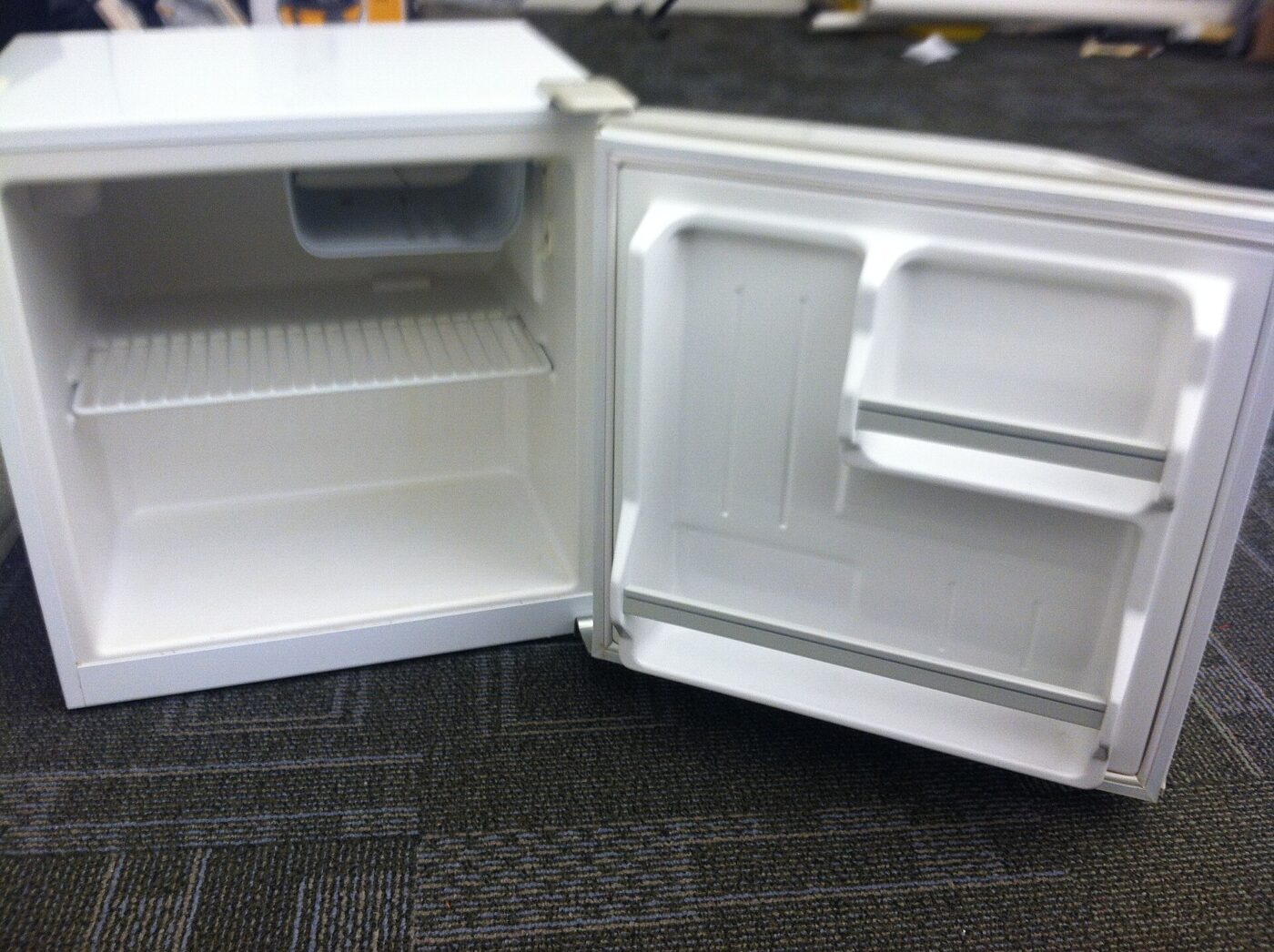 A compact refrigerator standing open, with a small lidded compartment above the wire shelf.