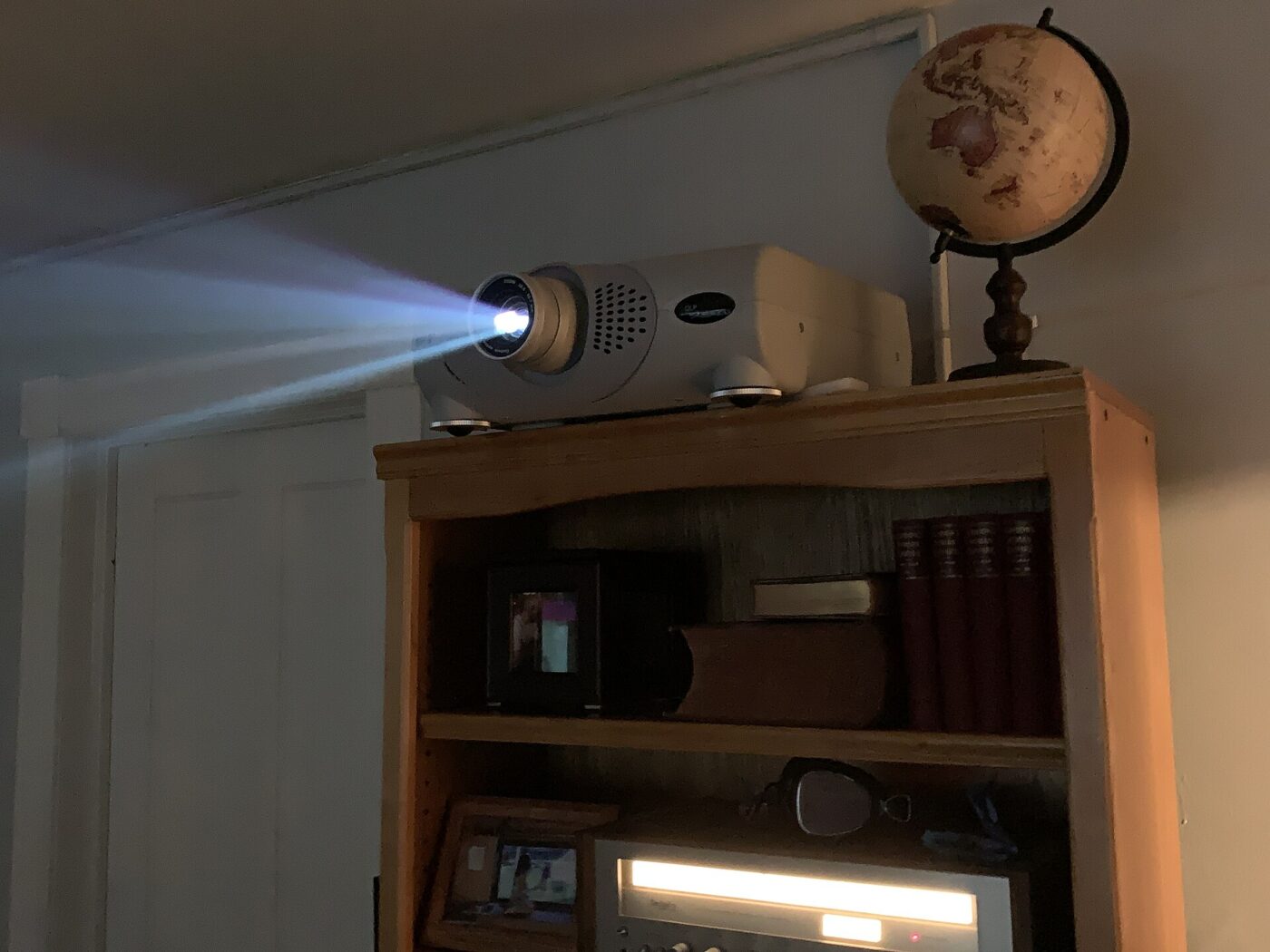 A home projector on top of a bookcase, its beam crossing a dim room.
