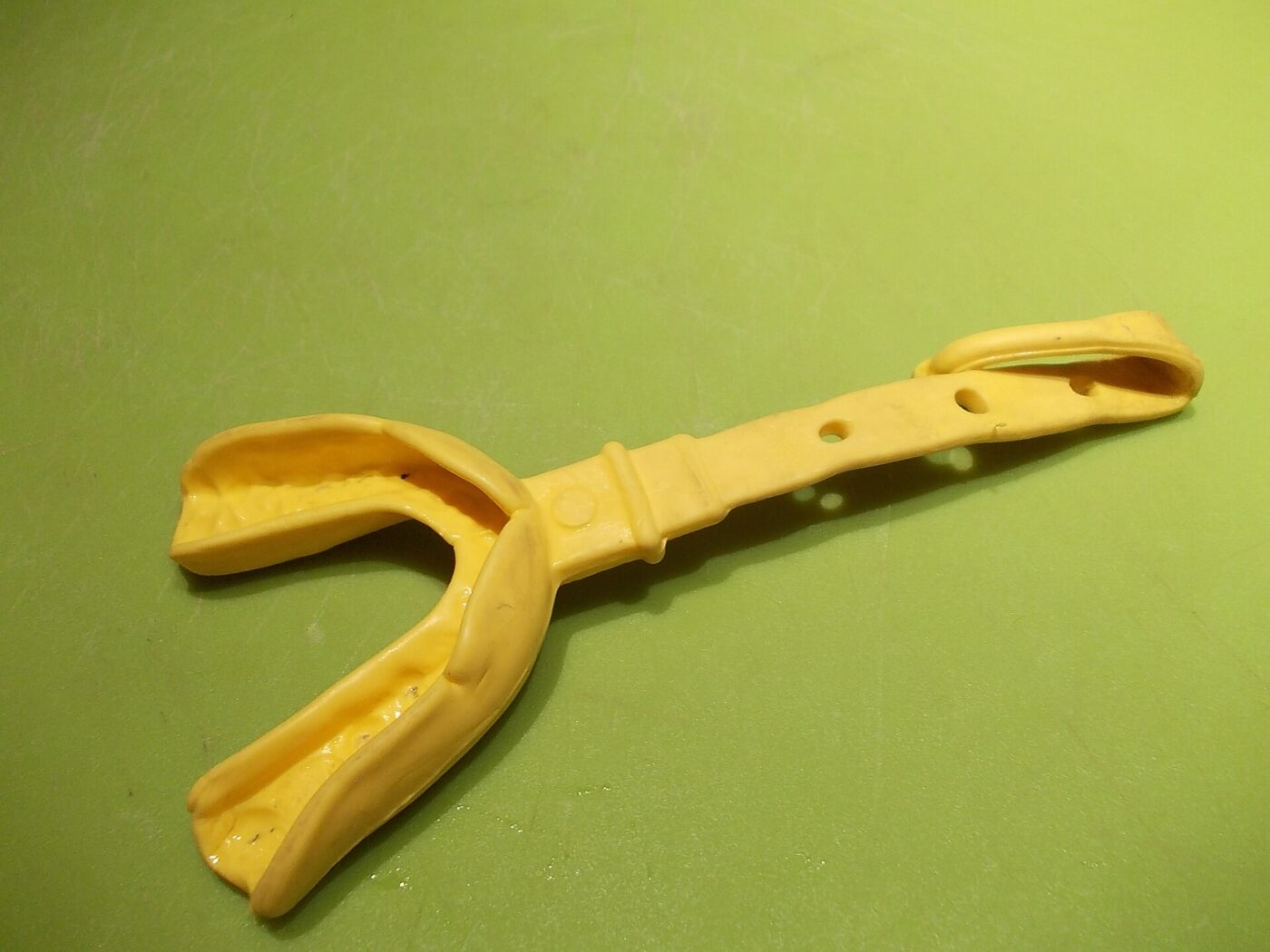 A yellow football mouthguard with its helmet strap attached, lying on a green background.