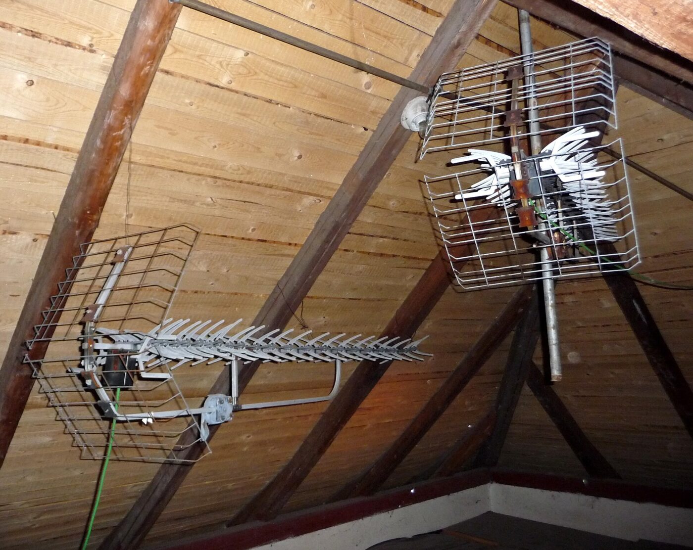 Two metal television antennas mounted in an attic under the roof rafters