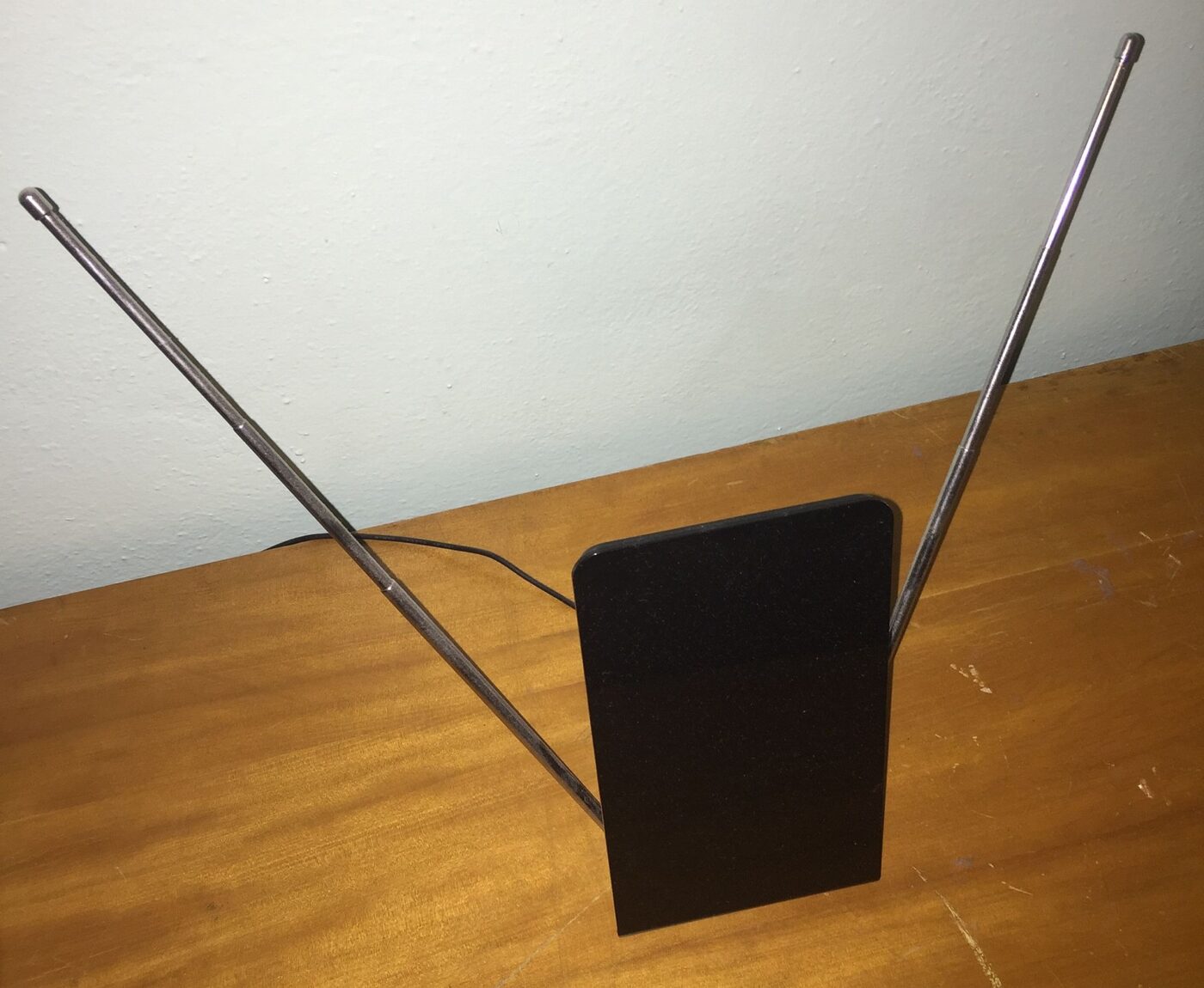 A flat indoor television antenna with two telescoping rods standing on a table