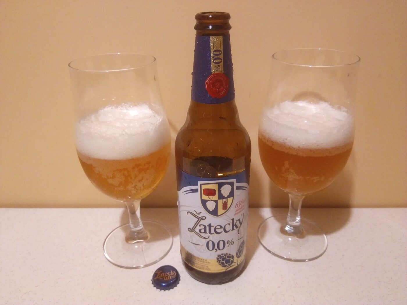 A bottle of 0.0% alcohol-free lager beside two stemmed glasses of poured beer