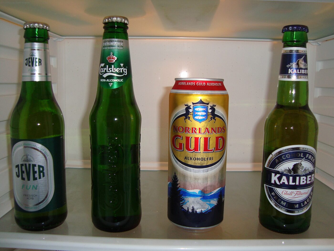 Four non-alcoholic beers, three in bottles and one in a can, on a refrigerator shelf